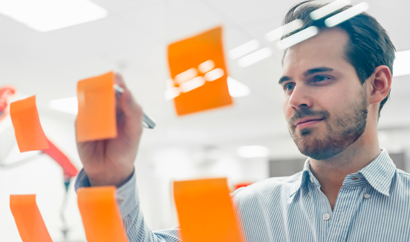 A Man Smiling And Sticking Orange Notes On A Glass Surface